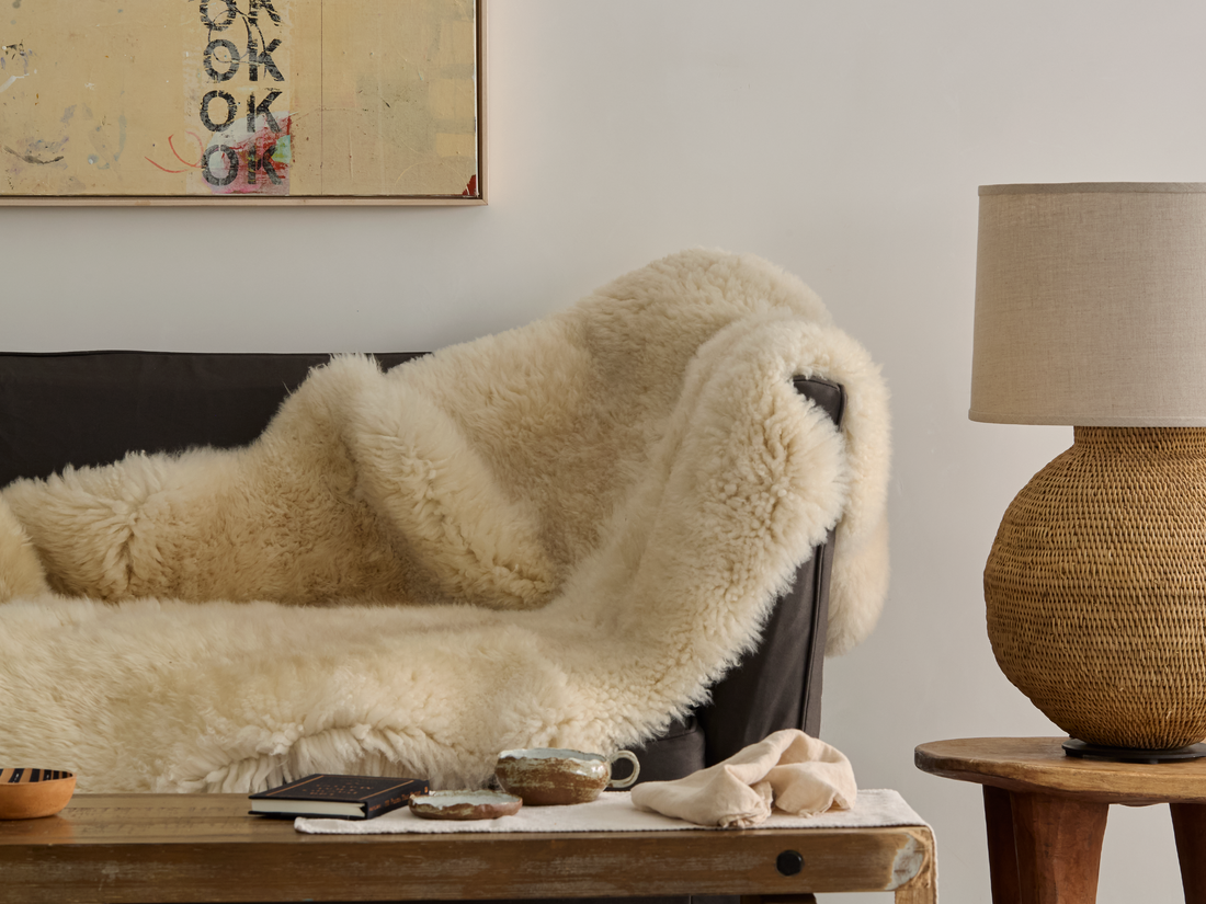 Cozy living room with a fluffy sheep skin blanket on a couch and a basket lamp on a side table.