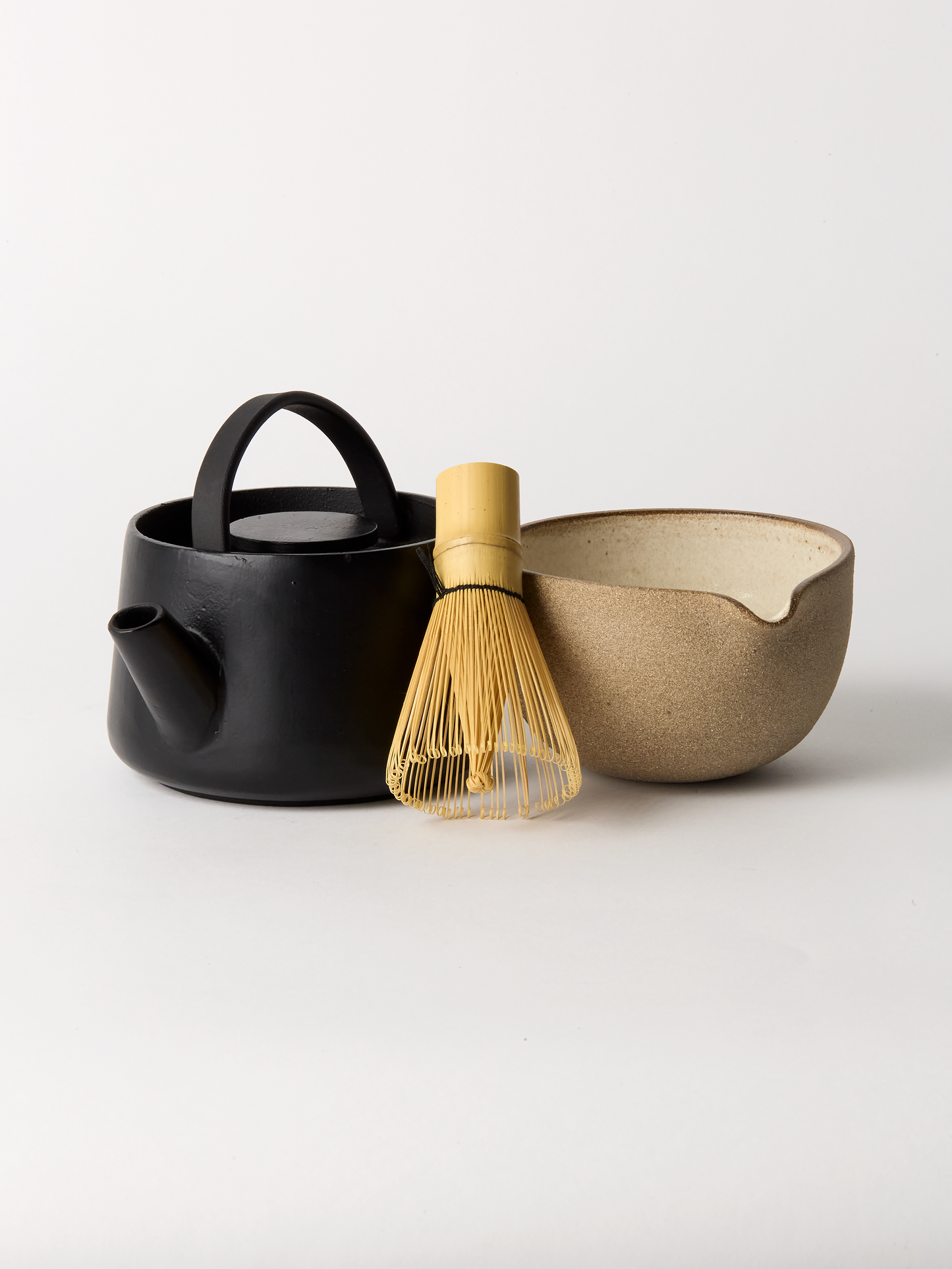Black teapot, bamboo whisk, and beige bowl on a white background